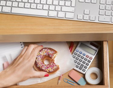 A woman's hand reaching for a doughnut in her desk drawer