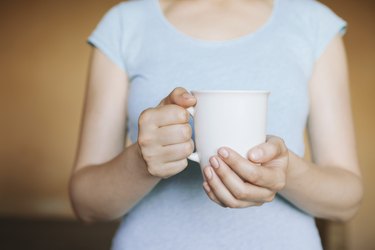 close view of a person in a blue t-shirt holding a white mug, to represent drinking hot water for weight loss