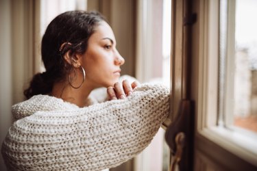 A woman with depression looking out the window of her home